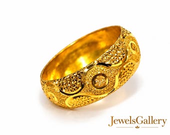 May include: A wide gold band ring featuring a textured surface with repeating circular patterns and polished gold accents. The ring has a high-shine finish and a detailed, embossed design across the entire outer circumference of the band.