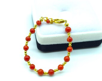 Puede incluir: Una pulsera de cuentas que alterna cuentas redondas de coral rojo con pequeñas cuentas espaciadoras de metal pulido en tono dorado. La pulsera cuenta con un cierre de mosquetón de metal dorado y una cadena extensora para ajustar el largo.