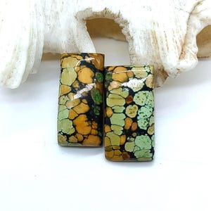 Puede incluir: Dos cabujones rectangulares con un patrón tipo mosaico de manchas verde claro, oliva y marrón dorado, separadas por líneas de matriz negras oscuras. Las piedras tienen una superficie lisa y pulida con un acabado brillante.