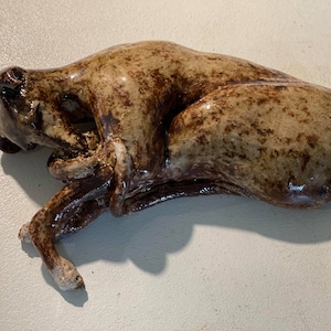 May include: A ceramic sculpture of a brown and white dog lying down with its head resting on its paws.