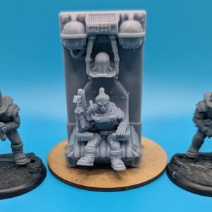 Op de afbeelding: Drie grijze plastic miniatuurfiguren, één zittend op een troon, de andere twee staand. De troon is een grijs plastic model met een verhoogde rugleuning en armleuningen. De figuren dragen allemaal futuristische bepantsering en helmen.