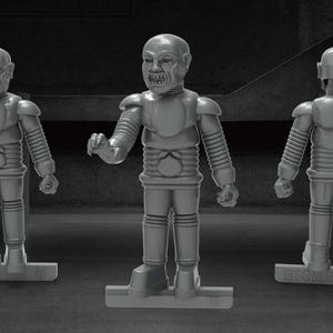 Może przedstawiać: Trzy szare figurki robotów o futurystycznym designie. Roboty mają ludzką formę z dużą głową i szczegółowym ciałem. Roboty stoją na szarej podstawie.
