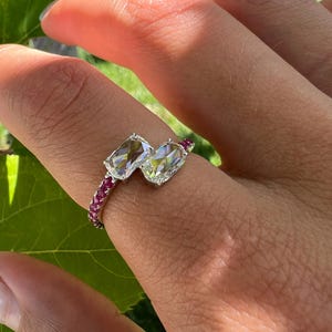 Può includere: Un anello bypass con due diamanti rettangolari taglio rosa montati su una fascia in metallo color argento. La fascia è impreziosita da una fila di piccoli rubini rosa brillante lungo il gambo, creando un netto contrasto con i diamanti sfaccettati.