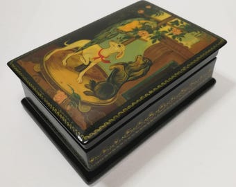 May include: A black lacquered box with a hinged lid, featuring a painting of two dogs. The artwork depicts a light yellow dog and a black dog in a room with floral details. The box is trimmed with gold.