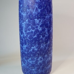 Op de afbeelding: Een blauwe keramische vaas met een gemarmerde, gevlekte glazuur. De vaas is cilindrisch van vorm en heeft een gladde, afgeronde rand.