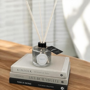 May include: A clear glass reed diffuser bottle with a black cap and several light-coloured reeds. A circular label reads FORTH OAK, and a black rectangular tag reads Reed Diffuser. The bottle sits atop a stack of three books titled KINFOLK, LIVE BEAUTIFULLY, and THIS IS HOME.
