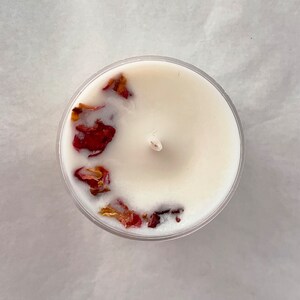 Puede incluir: Una vela blanca con p&eacute;talos de rosa secos incrustados en la cera. La vela est&aacute; en un recipiente de vidrio transparente.