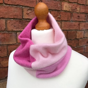 Peut inclure: Une écharpe en tricot infini rose et rose clair. L'écharpe est pliée et exposée sur un mannequin blanc.