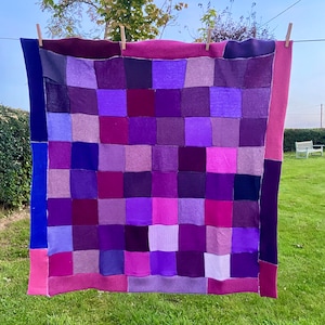 Peut inclure: Une courtepointe patchwork violette et rose avec un motif carré. La courtepointe est faite de différentes nuances de tissu violet et rose et est suspendue à une corde à linge.