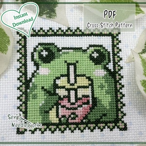 Puede incluir: Un patrón de punto de cruz con una rana verde sosteniendo una flor rosa. El patrón está enmarcado en un borde negro y verde con un diseño floral rosa y verde. El texto "PDF Cross-Stitch Pattern" está en la parte superior de la imagen.