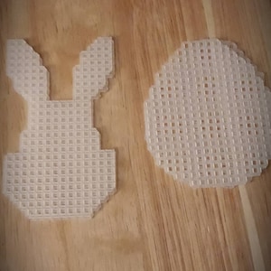 May include: Two white plastic canvas pieces, one shaped like a bunny and the other a circle. Both are made of a grid-like material.