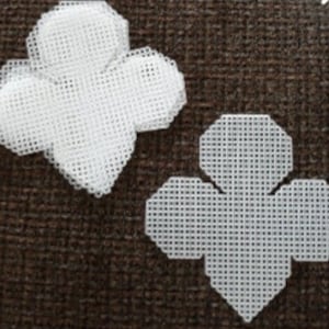May include: Two white plastic canvas shapes, each with a four-leaf clover design. The shapes are flat and have a grid pattern.