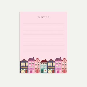May include: A pink notepad with the word "NOTES" at the top. The bottom of the notepad features a colourful illustration of a row of houses with various architectural details, including windows, doors, and decorative elements. The houses are in shades of purple, pink, blue, and green.