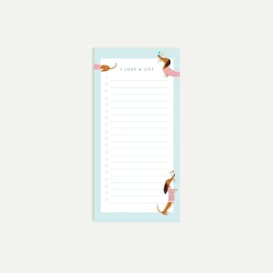 May include: A rectangular light blue notepad featuring the text "I LOVE A LIST" and a lined interior. The notepad is decorated with cartoon dachshunds wearing pink polka dot shirts and holding flowers.