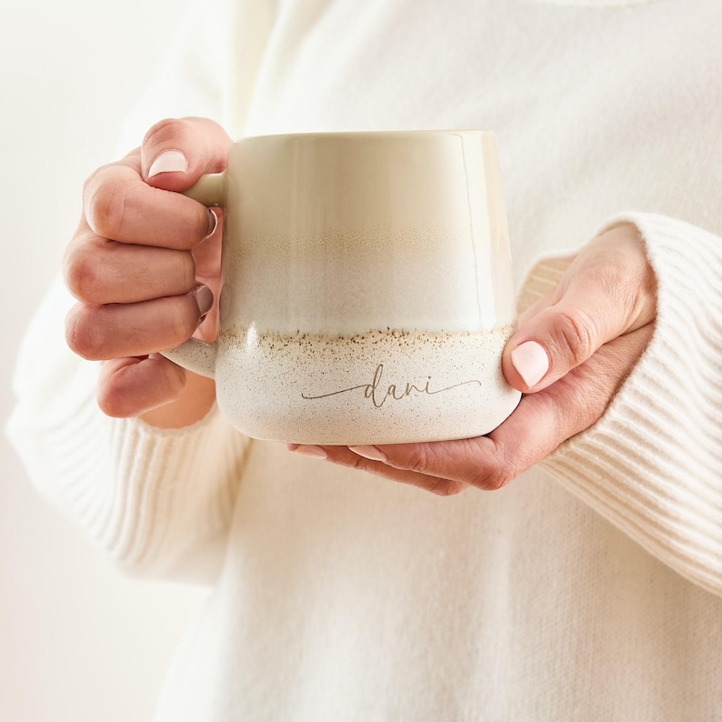 May include: A beige ceramic mug with a speckled glaze and a gold inscription that reads "dani".