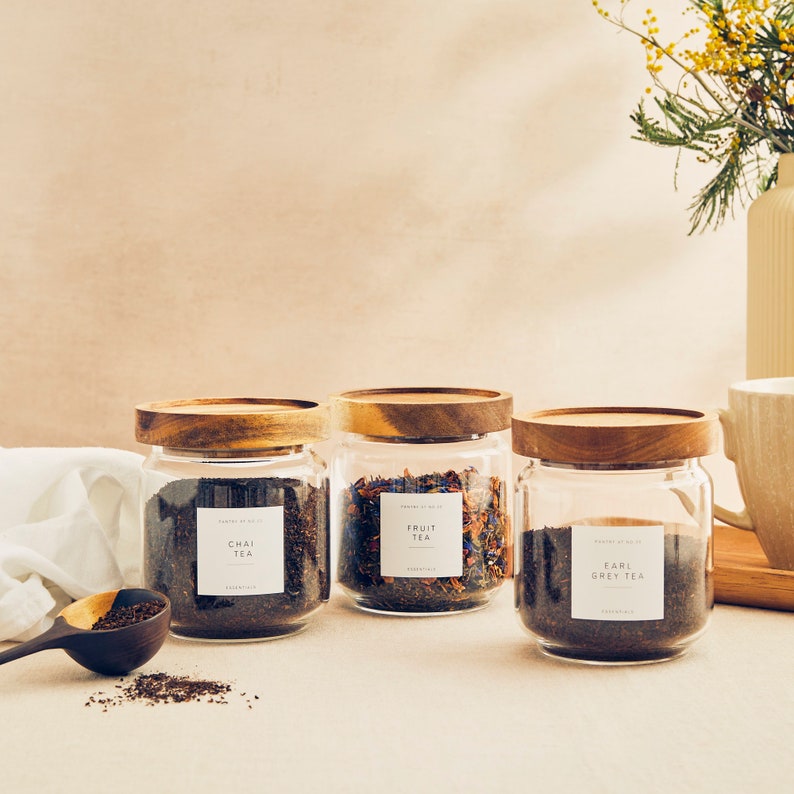 May include: Three glass jars with wooden lids filled with loose leaf tea. The jars are labeled "Chai Tea", "Fruit Tea", and "Earl Grey Tea".