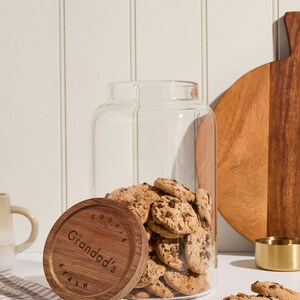 Peut inclure: Un pot &agrave; biscuits en verre avec un couvercle en bois. Le couvercle porte la gravure "Cookie Stash" et "Granddad's". Le pot est rempli de biscuits aux p&eacute;pites de chocolat.