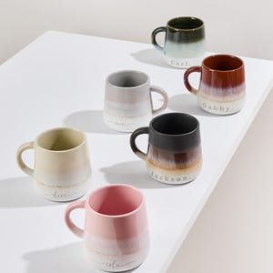 May include: Set of six ceramic mugs with ombre glaze and personalized names. The mugs are in various colors, including green, brown, gray, beige, black, and pink.