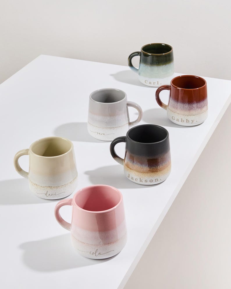 May include: Set of six ceramic mugs with ombre glaze and personalized names. The mugs are in various colors, including green, brown, gray, beige, black, and pink.