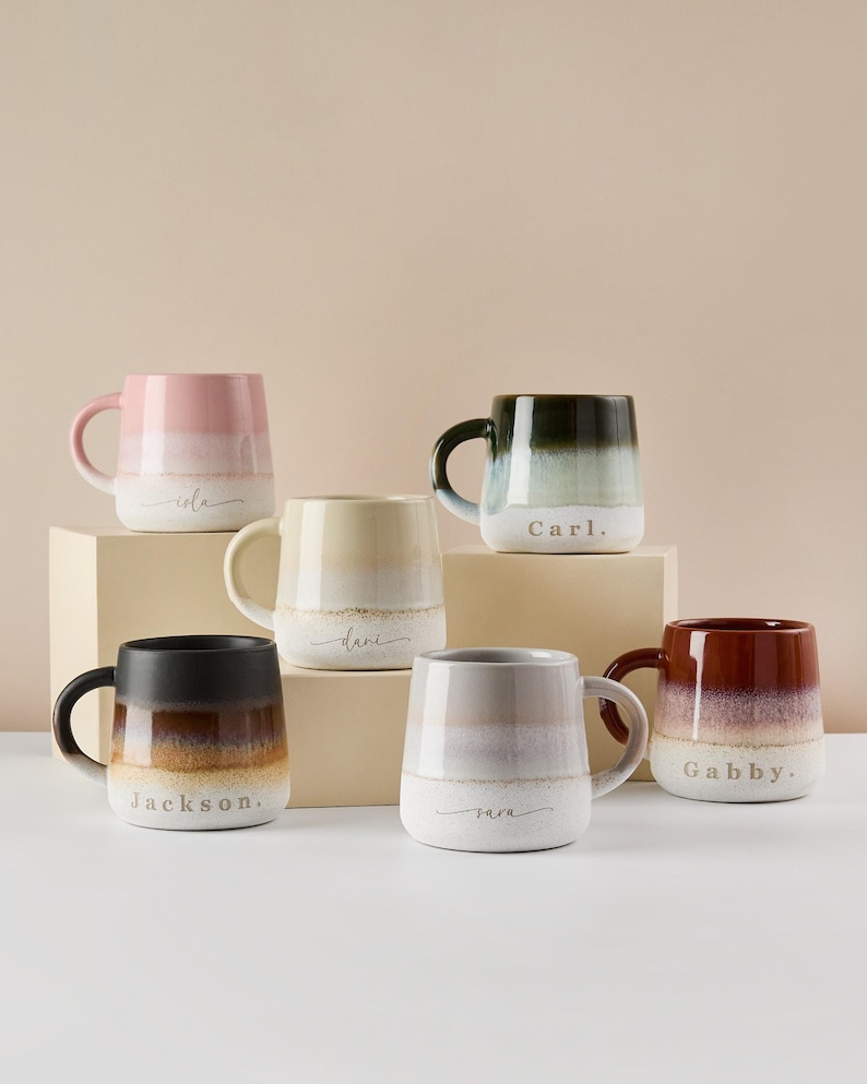 May include: Six ceramic mugs with ombre glaze in various colors. Each mug has a name written on the bottom in a cursive font. The names are: Lola, Dani, Carl, Jackson, Nara, and Gabby.