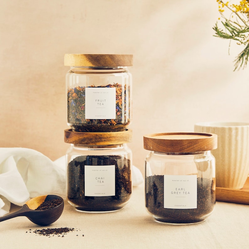May include: Three glass jars with wooden lids filled with loose leaf tea. The jars are labeled "Fruit Tea", "Chai Tea", and "Earl Grey Tea".