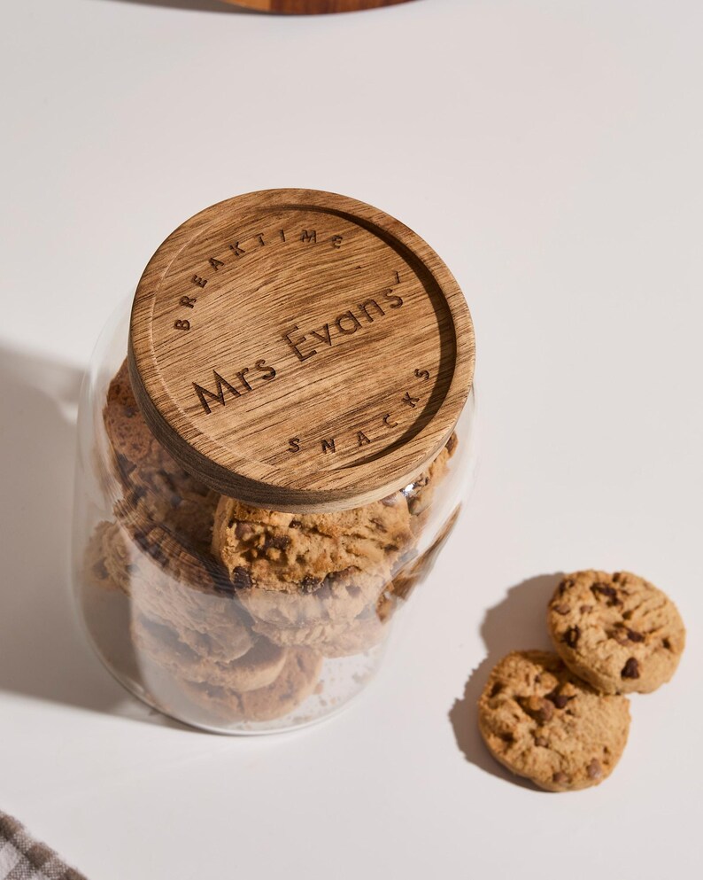 Peut inclure: Un bocal en verre avec un couvercle en bois rempli de biscuits aux p&eacute;pites de chocolat. Le couvercle porte la mention "BREAKTIME" et "Mrs. Evans" grav&eacute;e.