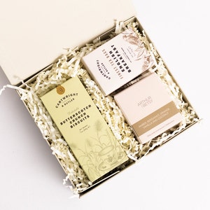 Op de afbeelding: Een cadeaudoos gevuld met bruin papierstrooisel, met drie items: een doos Butterscotch Crunch Biscuits, een doos Finest Tea Bags English Breakfast en een kaars met de naam Amber Bergamot Orange Vanille en Kokos.