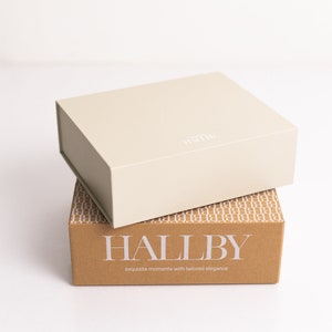 Pu&ograve; includere: Una scatola beige con la parola "HALLBY" stampata su di essa &egrave; impilata su una scatola marrone con il testo "HALLBY exquisite moments with tailored elegance".