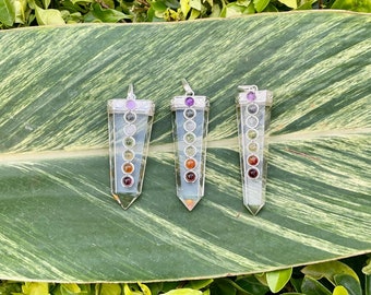 May include: Three silver pendants with clear quartz points and seven colored stones representing the seven chakras. The pendants are arranged on a green leaf.