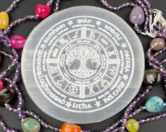 May include: A white selenite charging plate with a tree of life design and the eight sabbats of the Wheel of the Year inscribed around it. The plate is surrounded by a strand of amethyst beads with various colored gemstones.