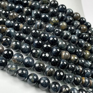 Può includere: Una collana di perle di occhio di tigre blu scuro. Le perle sono rotonde e hanno una finitura liscia e lucida. Le perle sono disposte in una fila, con la fila superiore che si sovrappone leggermente alla fila inferiore.
