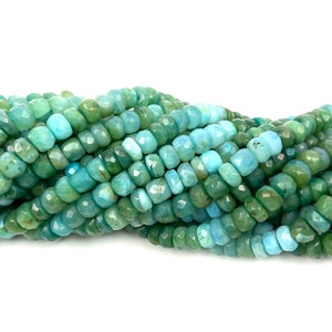 May include: A strand of faceted turquoise blue and green gemstone beads. The beads are all approximately the same size and shape, and they are strung together on a clear thread.