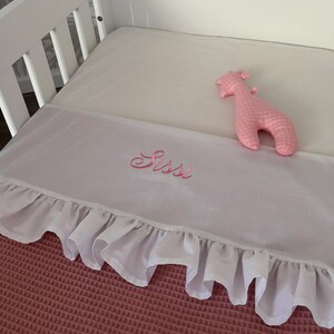 Spannbettlaken für Kinderbett mit Rüschen und aufgesticktem Babynamen. Bettlaken mit Rüsche.