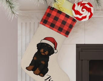 Op de afbeelding: Een kerstsok met een zwart-rode buffelruitmanchet en een crèmekleurig lichaam. De sok heeft een afbeelding van een zwarte en bruine puppy met een kerstmuts, met de naam "Ziggy" eronder gedrukt. Een rood-witte swirl lolly is bevestigd.