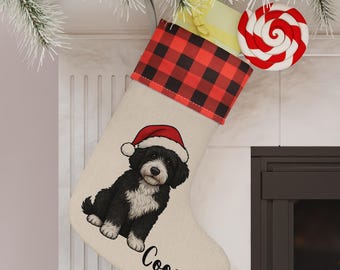Op de afbeelding: Een kerstsok met een zwart-witte hond met een kerstmuts. De sok heeft een rood-zwarte geruite manchet en de naam "Cooper" erop gedrukt. Een rood-witte lolly is bevestigd.