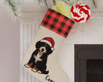 Op de afbeelding: Een kerstsok met een rode en zwarte buffelruitmanchet, met een puppy met een kerstmuts. De sok is gepersonaliseerd met de naam "Cooper". Een rood-witte spiraallolly is bevestigd.