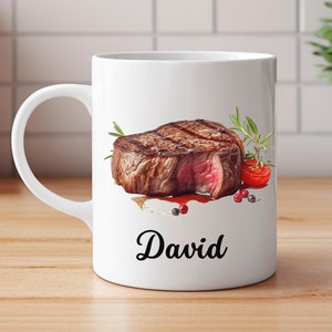 Op de afbeelding: Witte keramische mok met een afbeelding van een gegrild biefstuk, kruiden en een rode paprika. De mok heeft de naam "David" onderaan gedrukt.