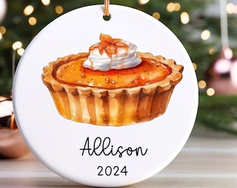 Peut inclure: Ornement de Noël rond et blanc avec une illustration à l'aquarelle d'une tarte à la citrouille garnie de crème fouettée. L'ornement a une ficelle dorée pour l'accrocher et le nom "Allison" et l'année "2024" imprimés.