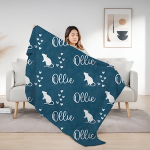 May include: A blue fleece blanket with a white rat and the name "Ollie" repeated throughout the design. The blanket is being held by a person.