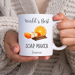 May include: White ceramic mug with a black and orange design. The mug reads "World's Best Soap Maker Jessica".