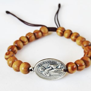 May include: A brown wooden beaded bracelet with a silver oval charm featuring the image of Saint Francis of Assisi. The charm has the text "Saint Francis" inscribed on it.