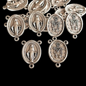 May include: Silver-toned metal charms with a religious theme. The charms feature an image of the Virgin Mary and the words "Regina Sine Labe Original Conception".