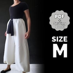 May include: A white pair of wide-leg pants with a black fabric belt. The pants have a gathered look at the bottom. The model is wearing a black short-sleeved shirt. The image also includes the text "PDF + Sewing Book" and "SIZE M".