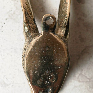 May include: A brass wall hook shaped like a bird with its wings spread out. The hook is designed to be mounted on a wall and has a small hole at the top for hanging.