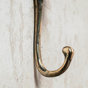 May include: A close-up of a gold-toned metal hook. The hook is curved and has a rounded end.