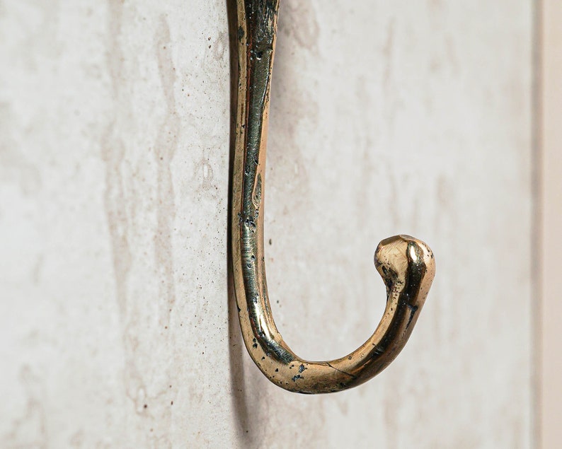 May include: A close-up of a gold-toned metal hook. The hook is curved and has a rounded end.