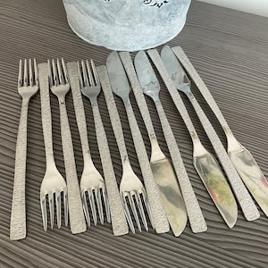 May include: A set of silver cutlery, including forks and knives, with textured handles. The cutlery is arranged in a row on a wooden surface.