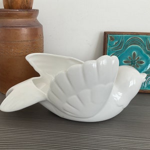 May include: White ceramic bird planter with a wing-shaped opening. The planter is shaped like a bird in flight with its wings spread out.