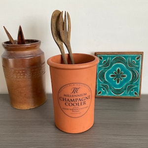 May include: A terracotta champagne cooler with the text "The Suffolk Collection, Millennium Champagne Cooler, Made by Henry Watson's Pottery, England, 1999" printed on the side.