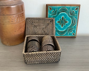 May include: A woven wicker box with a lid, containing two smaller woven wicker boxes. The box is brown and has a natural finish. The box is sitting on a gray surface.